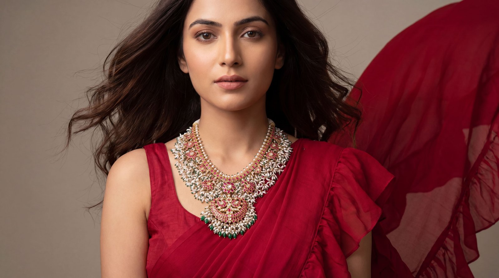 AI jewellery photography: a model in a red saree wearing a gold necklace set with pearls and pink stones, red fabric moving behind her.